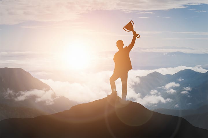 Silhouette of person on mountain top with trophy