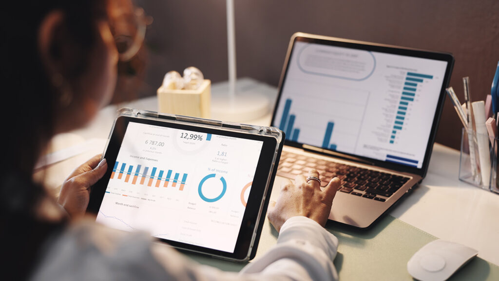 Woman looking at statistics on a tablet and laptop simultaneously