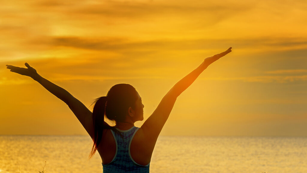 Silhouette of a woman raising her arms during a sunrise