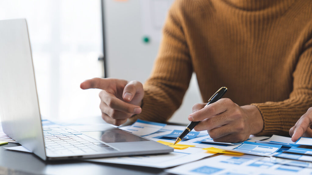 Person in a sweater pointing at a laptop screen