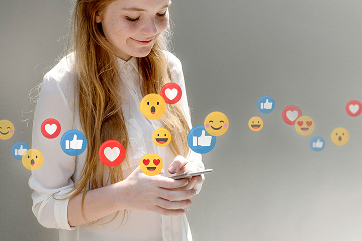 Girl smiling while looking at phone with emojis floating across middle of image