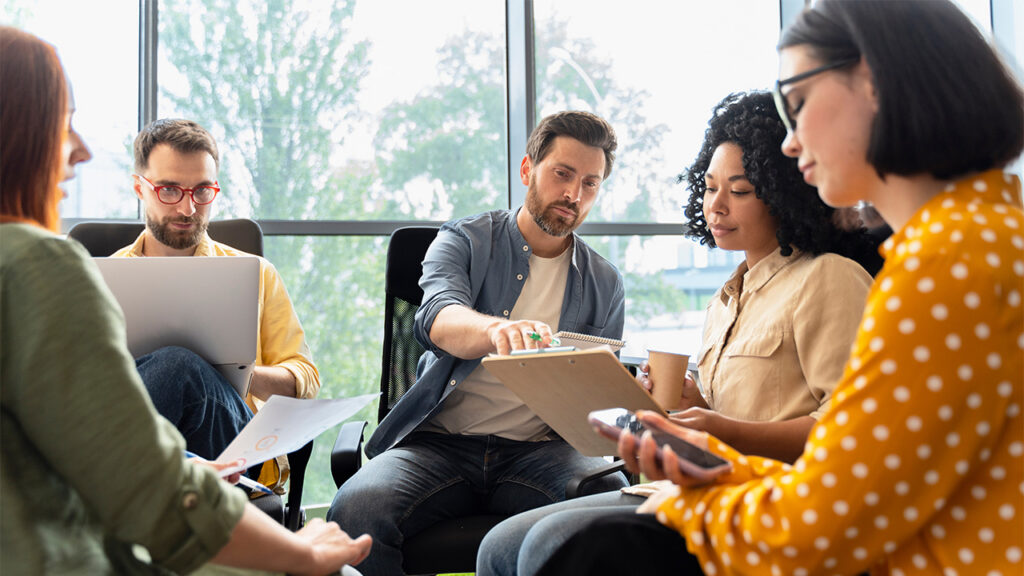 Image of a group of people sitting in a circle and looking at printed pages and tablets